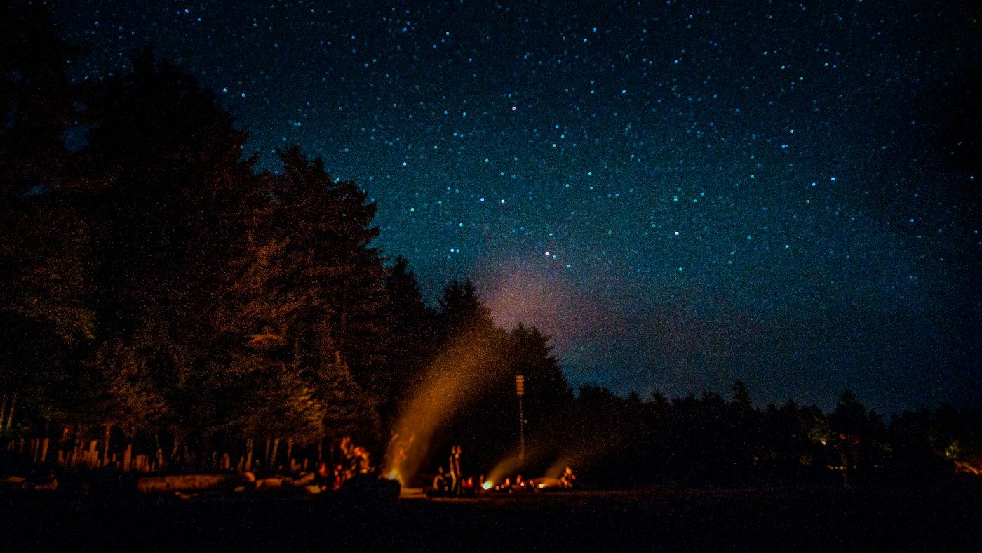 Grupo alrededor de una hoguera de noche bajo un cielo estrellado