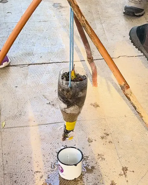 Filtro de agua casero hecho con una botella colgada de un trípode de palos