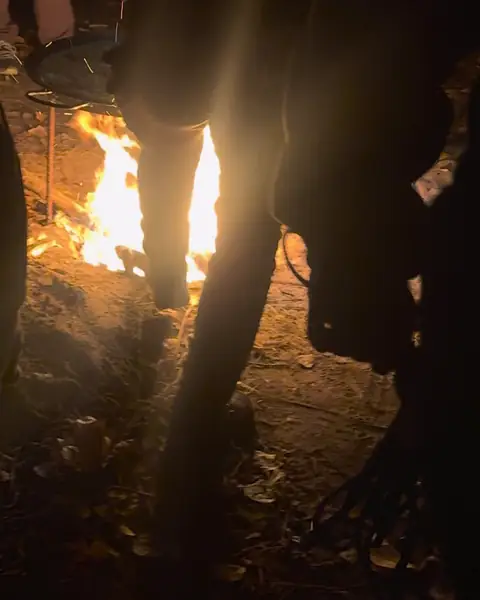 Hoguera encendida de noche en el campamento, con participantes alrededor