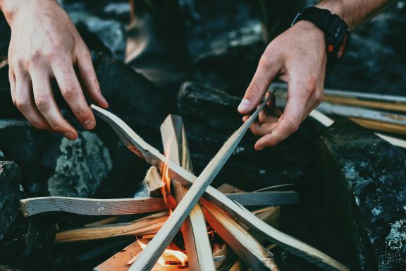 Tipología de fogatas Manos arreglando ramas sobre una fogata encendida.