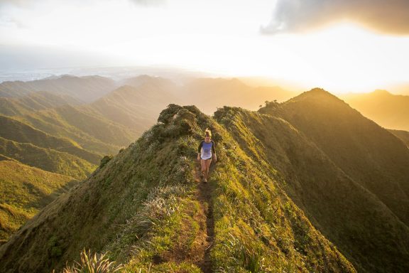 Trekking y Orientación en la Montaña Persona caminando por una cresta montañosa al atardecer, con vistas panorámicas.
