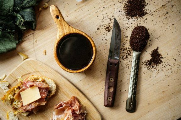 BushCraft Tostada con mantequilla, jarra de salsa, cuchillo y café molido sobre una mesa de madera.