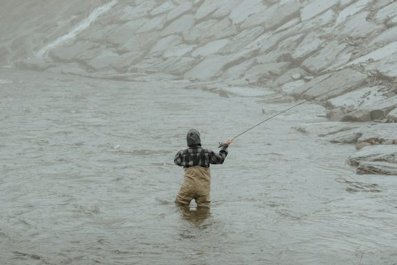 Pesca de Supervivencia Hombre pescando en un río, de pie en el agua con caña de pescar.